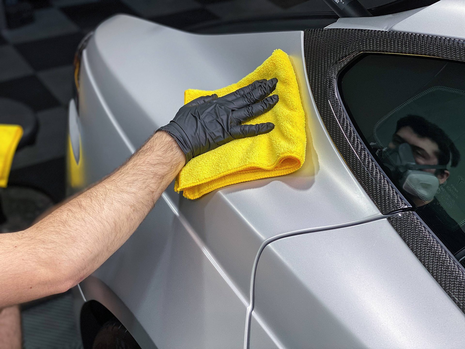 Gloved hand levelling coating on a silver panel with a yellow microfibre cloth