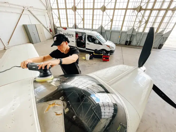 Detailer machine-polishing the nose of a white single-engine aircraft in a hangar