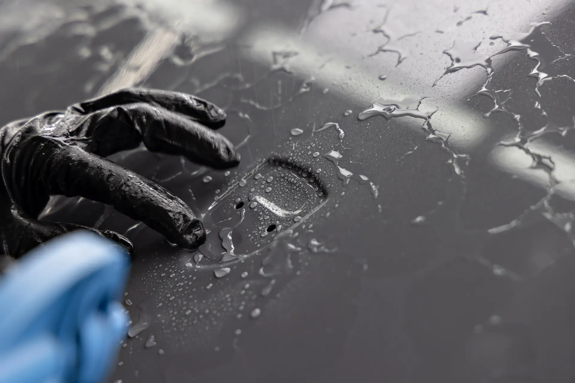 Gloved hands smoothing wet paint protection film across a dark grey body panel with a squeegee