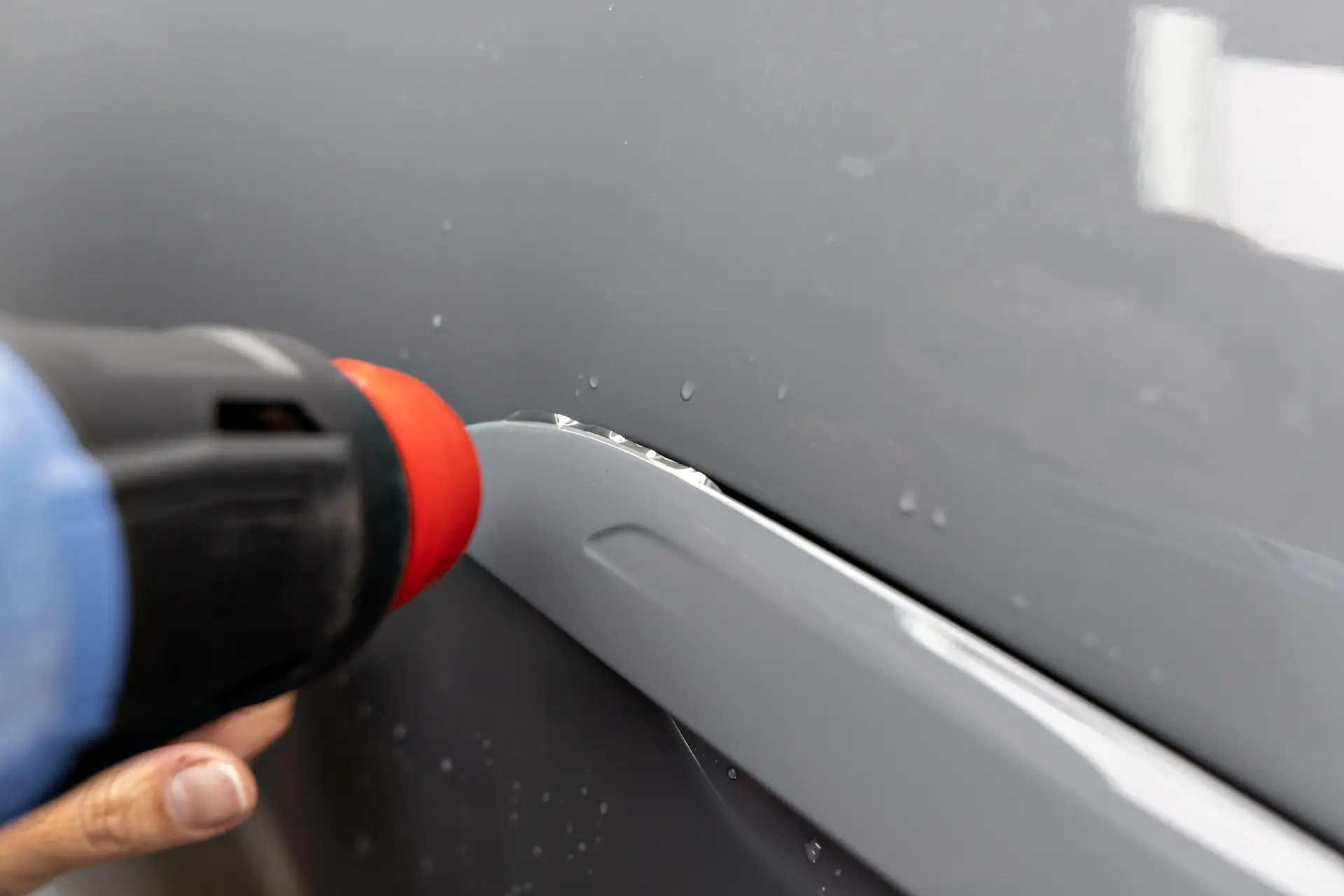 A heat tool being run along the wrapped edge of paint protection film on a grey body panel