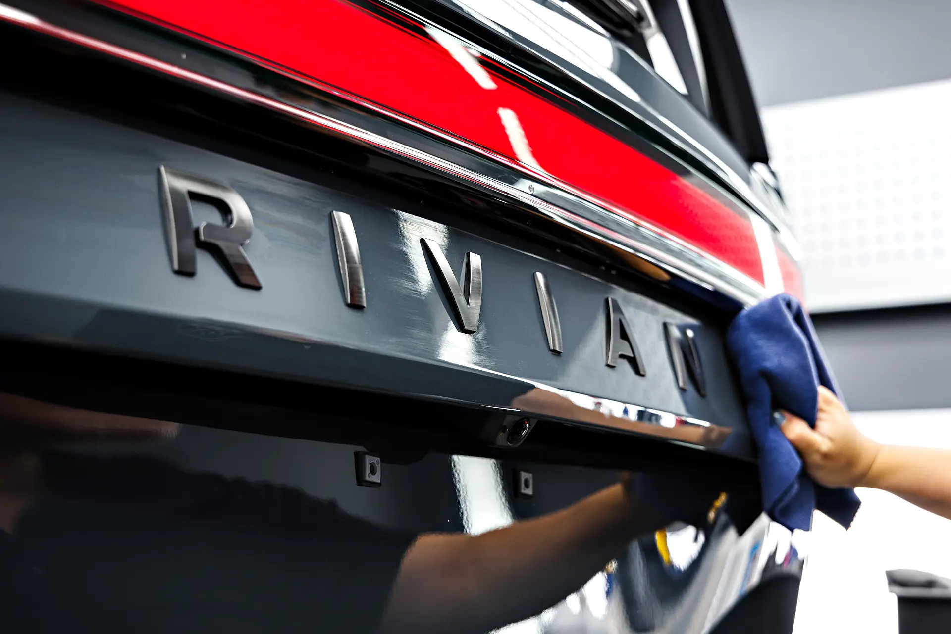 Gloved hand wiping the rear tailgate of a Rivian with a blue microfibre cloth
