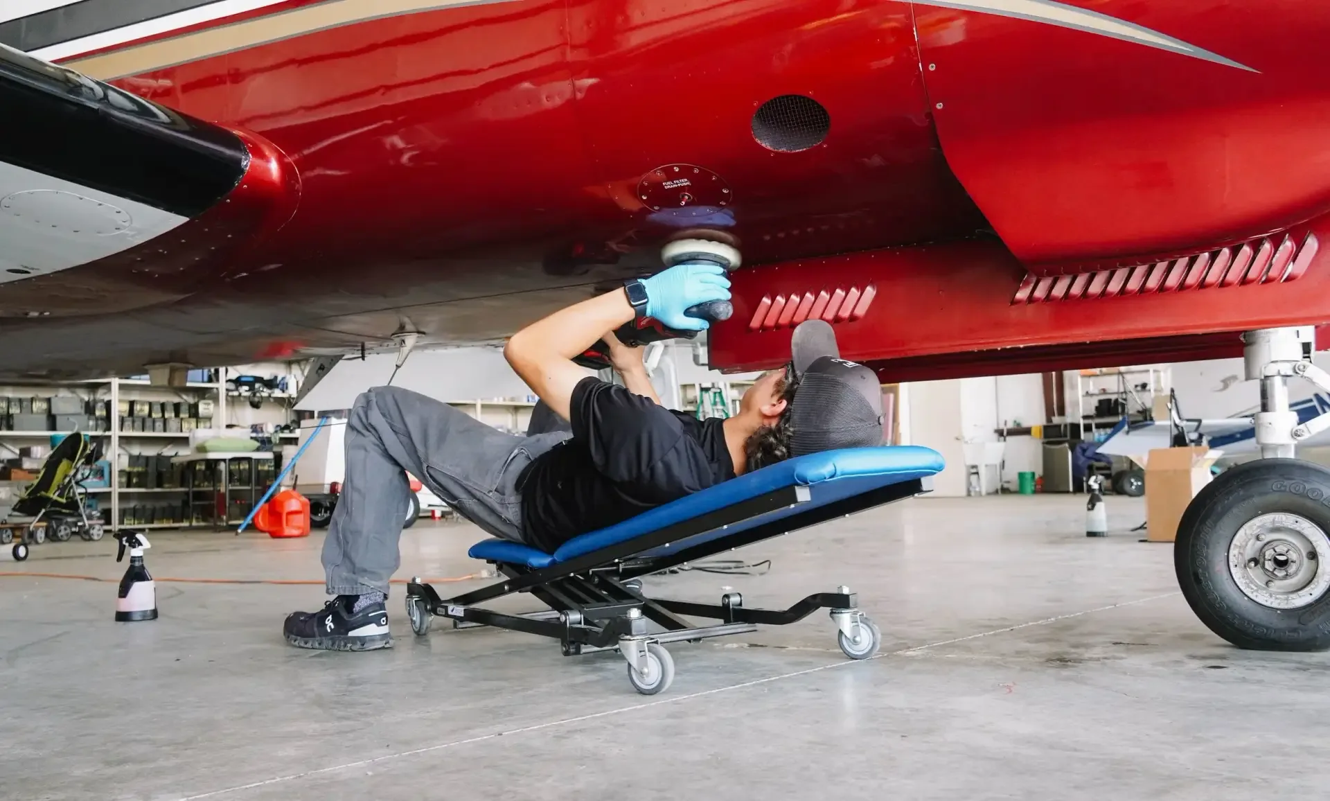 Detailer on a creeper polishing the underside of a red and white aircraft