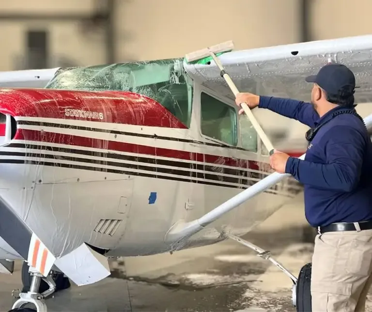 Detailer washing the wing of a red and white Cessna by hand with a long brush
