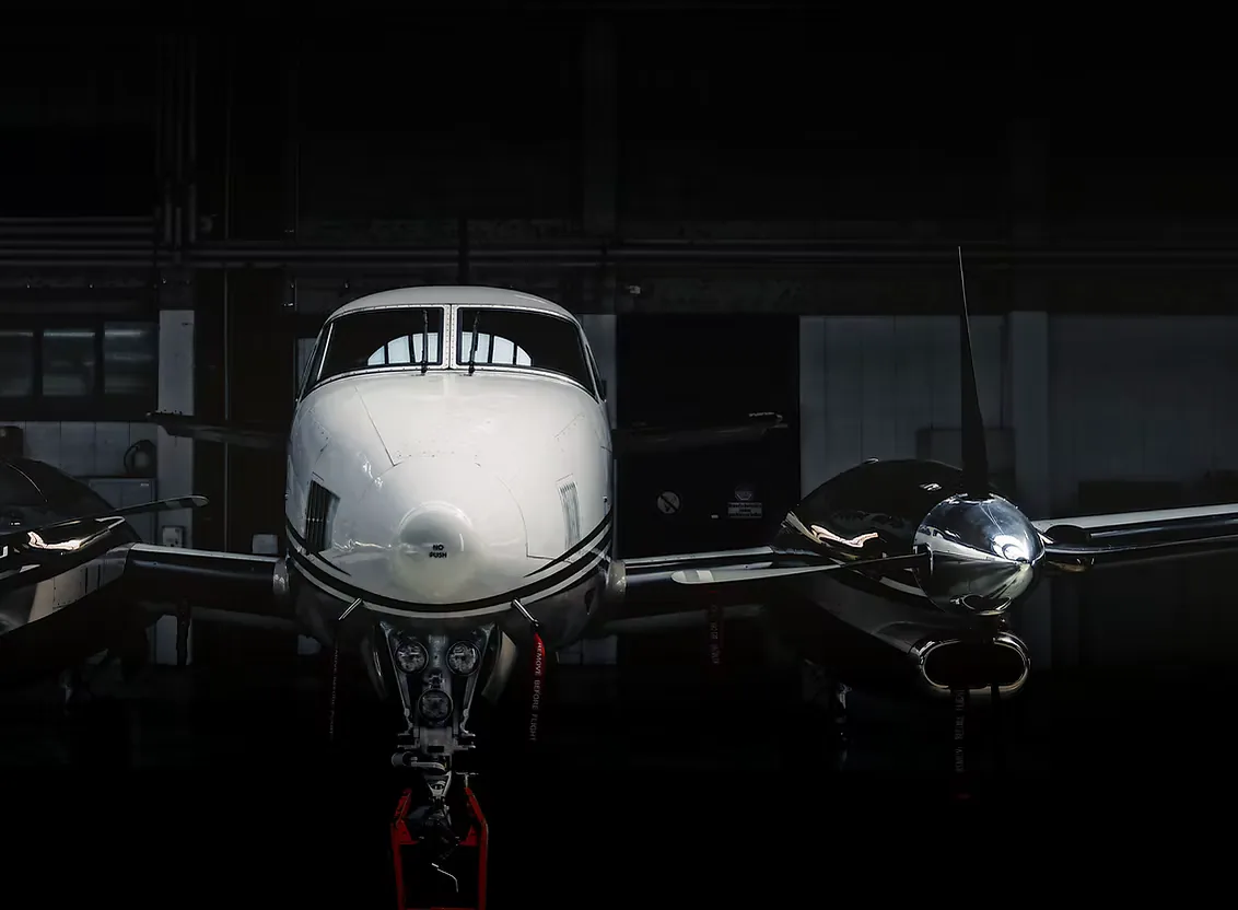 Nose of a white turboprop with its propellers, lit in a dark hangar