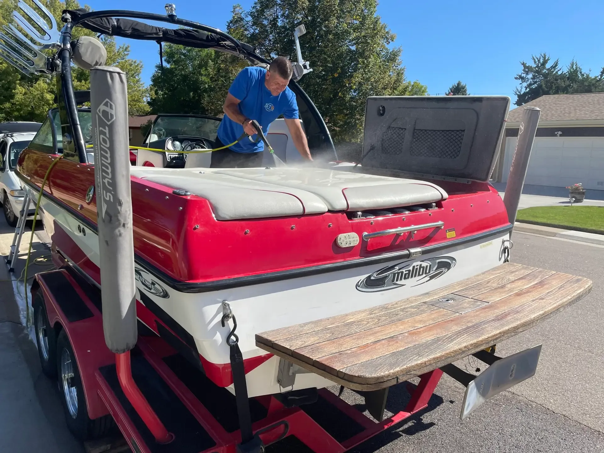 Technician in a blue shirt cleaning the deck of a red and white Malibu on its trailer, swim platform in the foreground