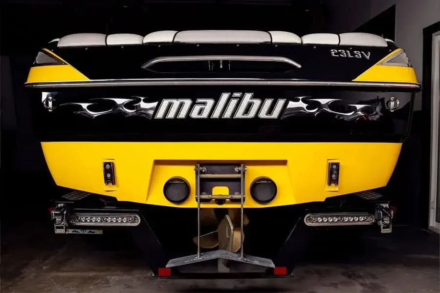 Stern of a black and yellow Malibu wake boat on its trailer in a dark garage