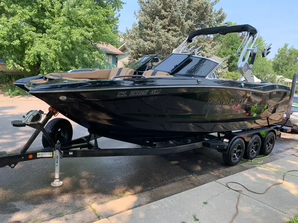 Black wake boat with a tower on its trailer in a driveway after an ST6 detail