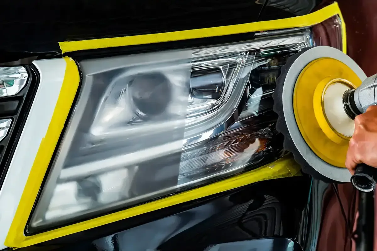 Headlight lens taped off while a machine pad refinishes it during ST6 headlight restoration