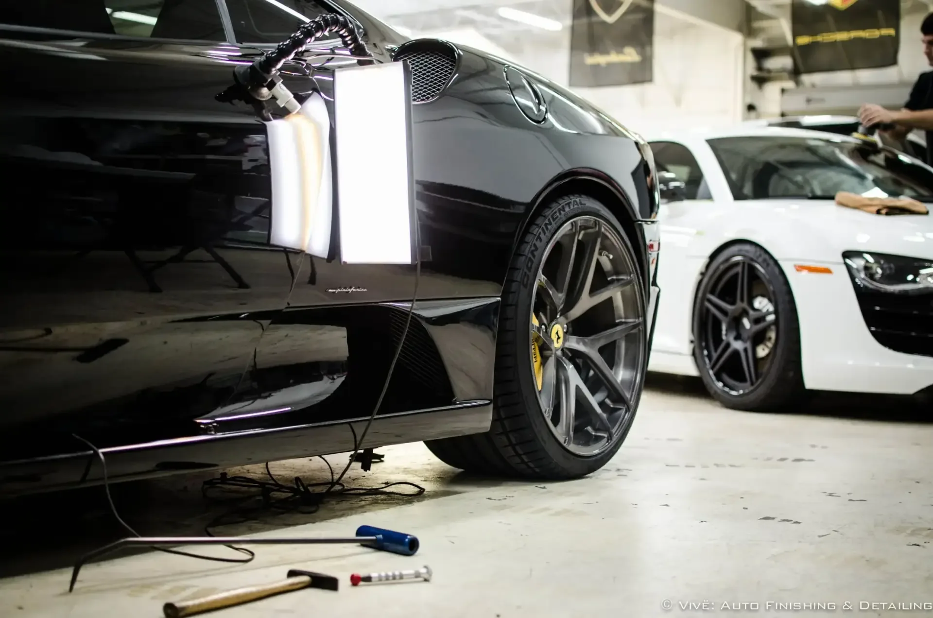 Black sports car on a lift with inspection lights aimed at the lower door during paint correction