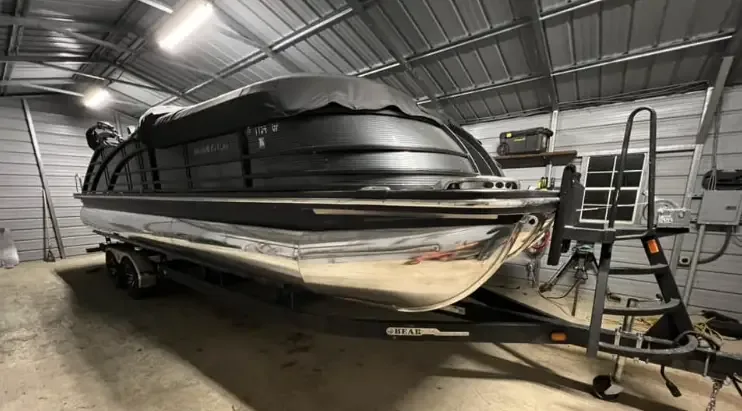 Black pontoon boat with mirror-polished aluminium logs on its trailer inside a shop