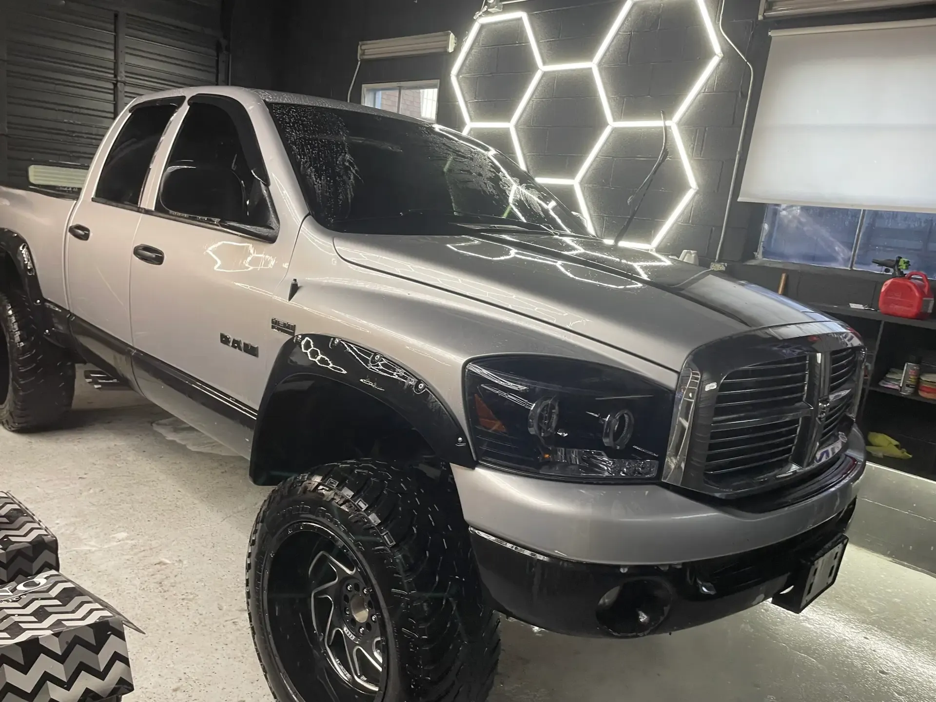 Lifted silver Dodge Ram pickup on aftermarket wheels under the hexagon LED lighting in the ST6 Detailers bay