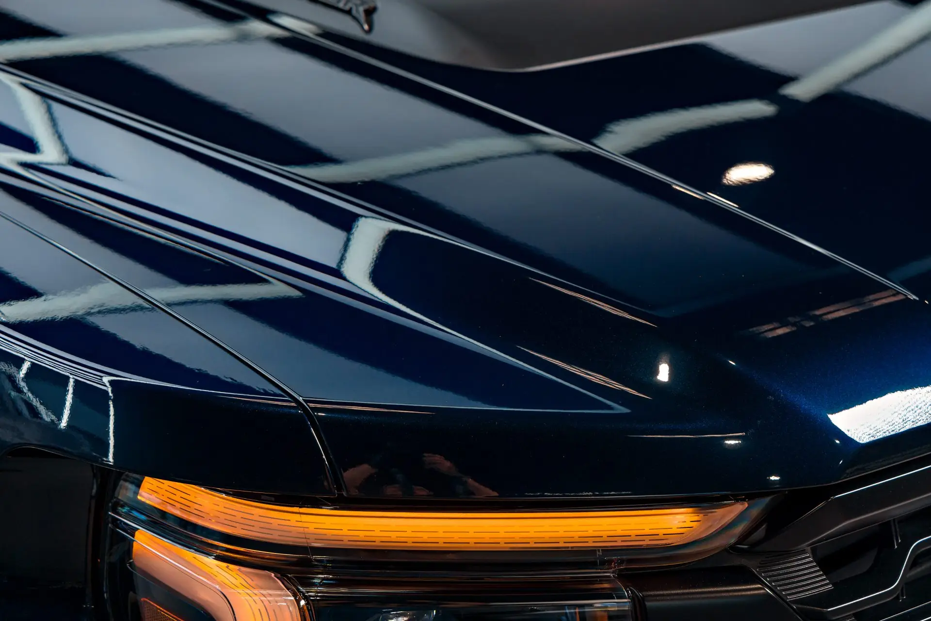 Hood and fender of a dark blue Ford Raptor with straight overhead light reflections in deep gloss