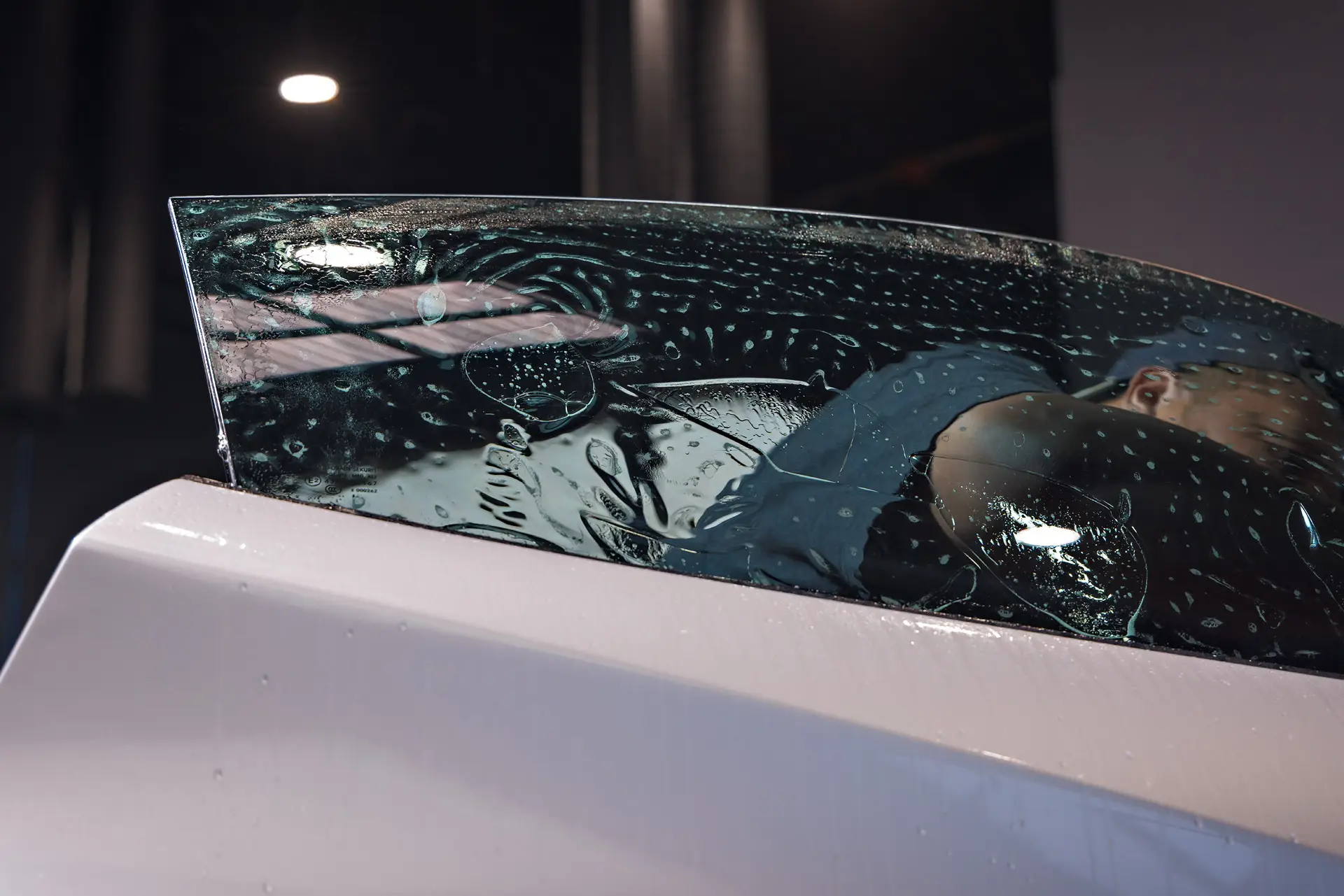 A curved sheet of dark window film laid over a white panel with slip solution beaded across it, under the shop lights