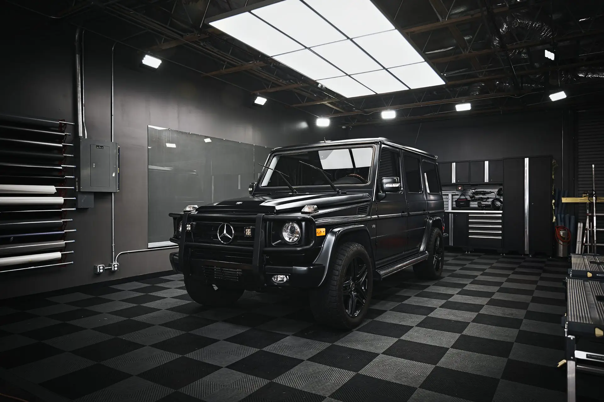 Black Mercedes G-Wagon parked in a dark garage with lit tool cabinets behind