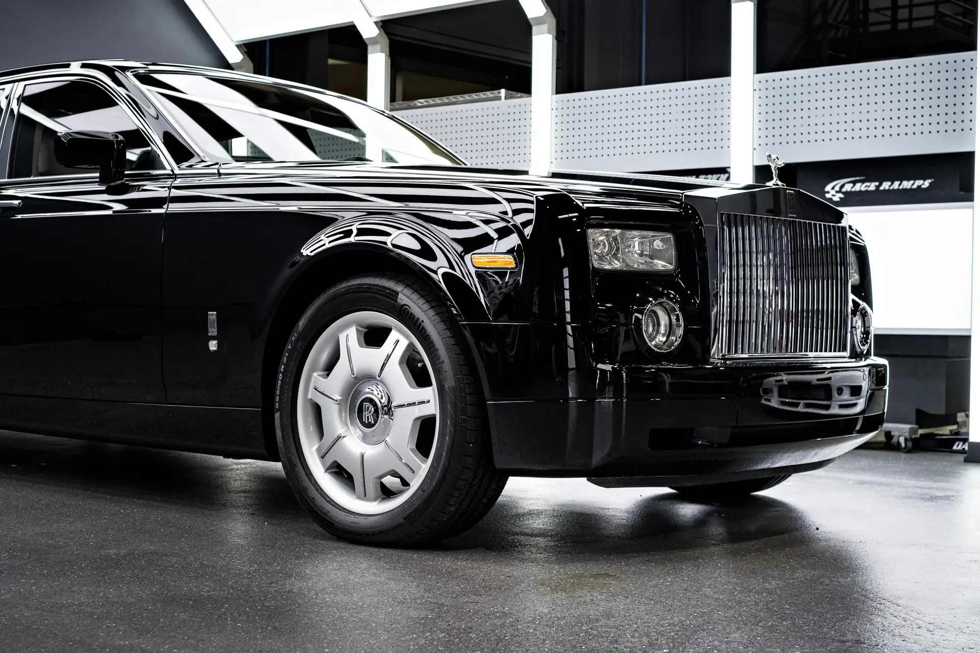 Front of a black Rolls-Royce Phantom with its chrome grille and polished wheel under dark studio lighting