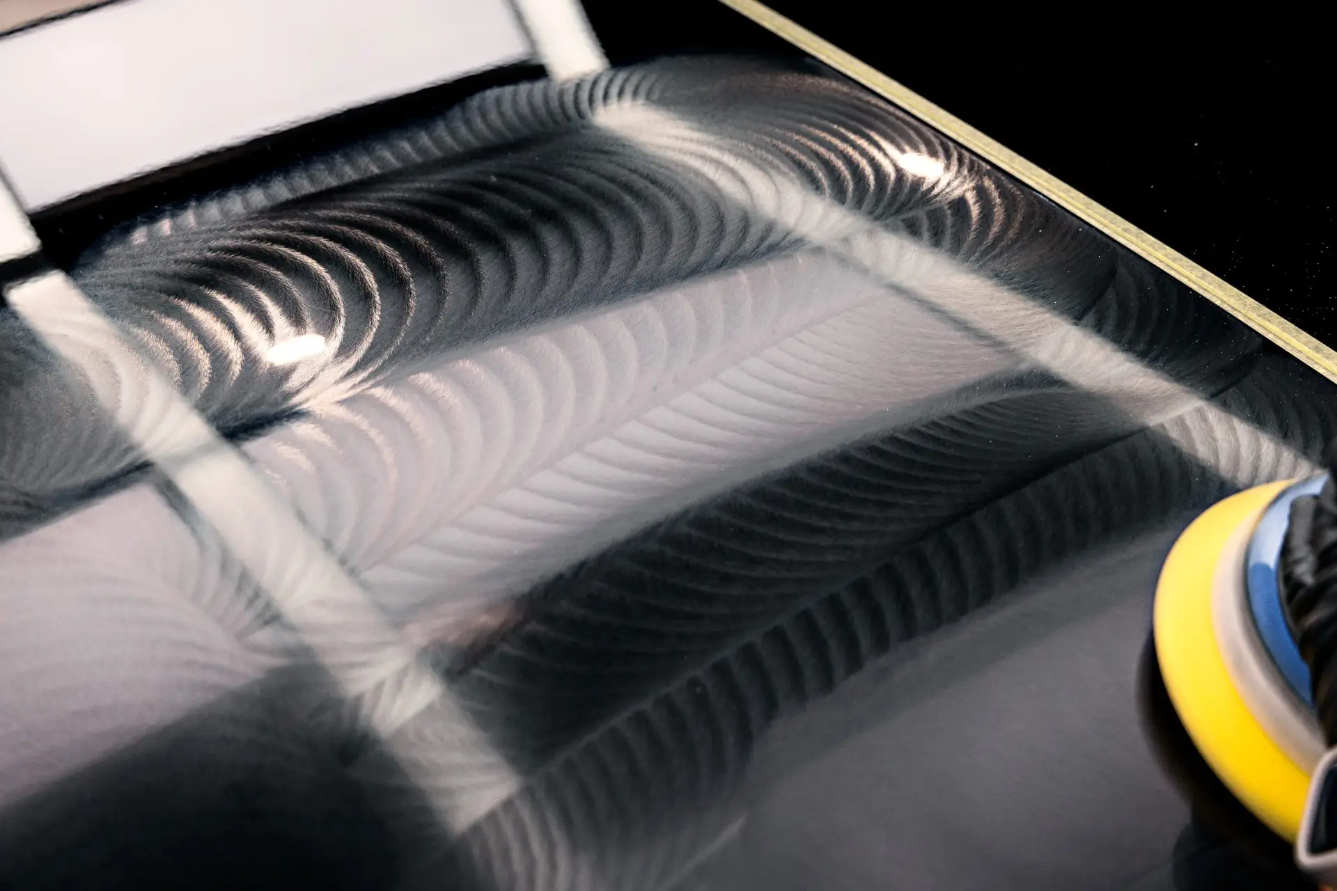 Black paint under a single light showing fine circular swirl marks before correction