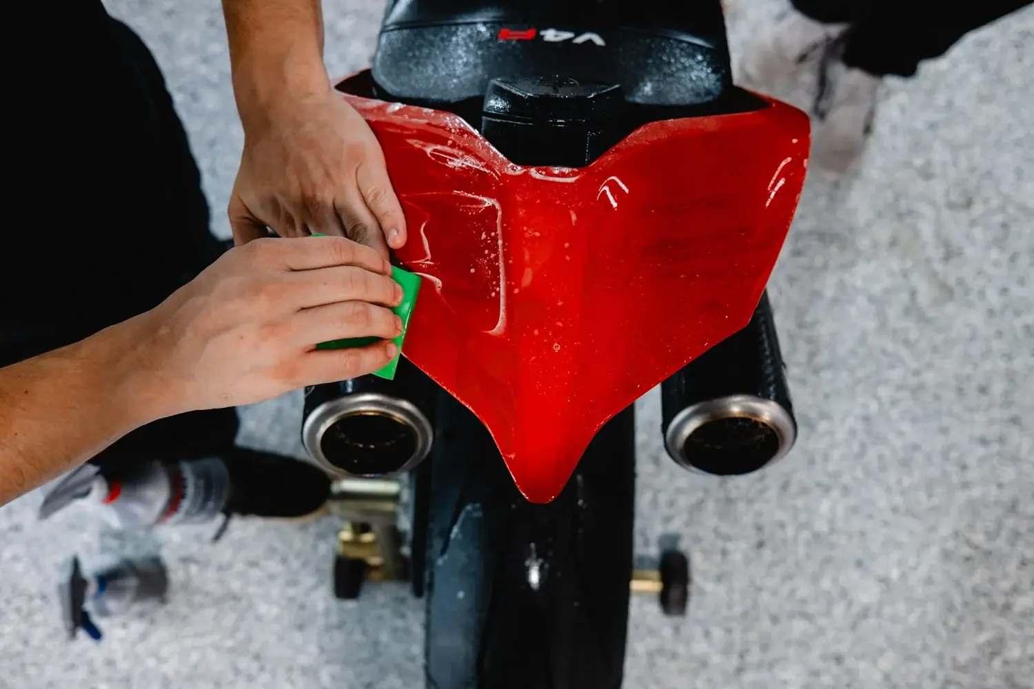 Hands working paint protection film onto the red tail section of a Ducati Panigale V4 R with a green squeegee