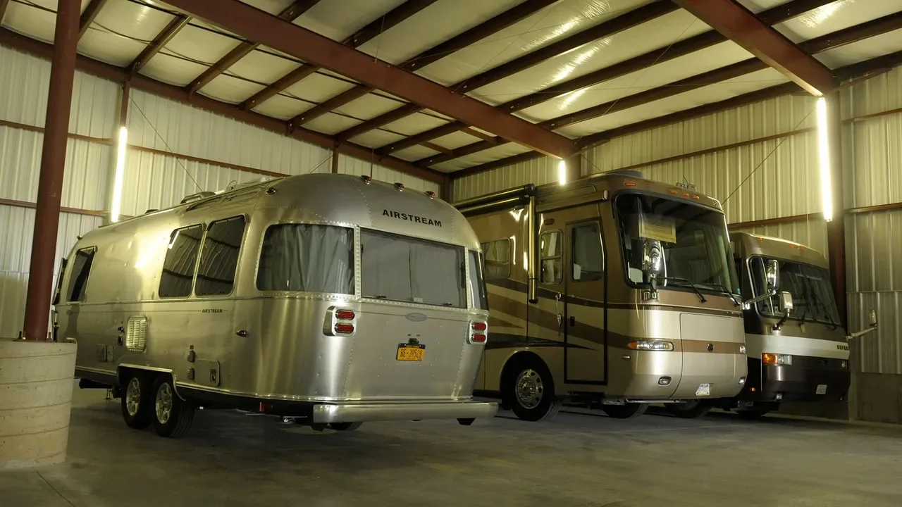 Silver Airstream travel trailer and two Class A motorhomes parked inside a metal storage building