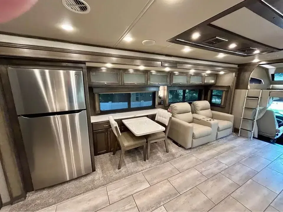Motorhome living area with a stainless fridge, dinette and two cream recliners on a tiled floor