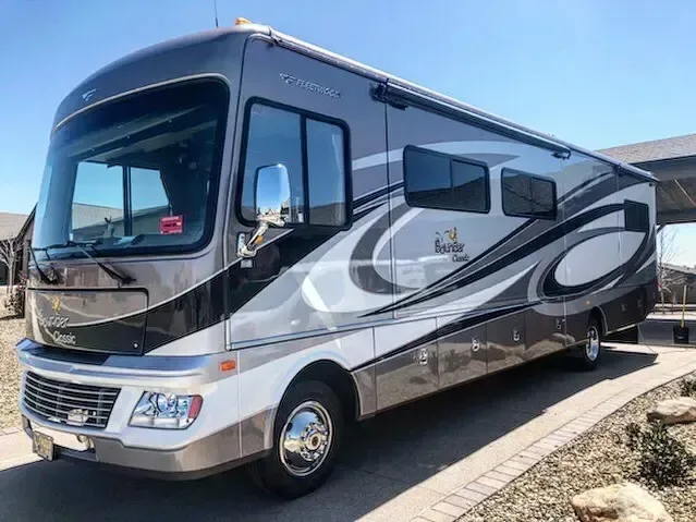 Silver Class A motorhome with grey swoosh graphics parked on a paver driveway