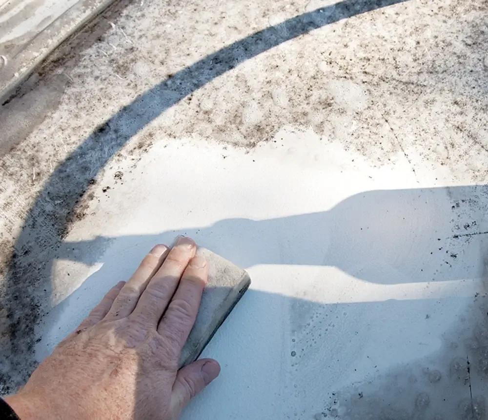 Hand scrubbing a stained white RV roof with a pad, dirt streaks visible around the cleaned patch