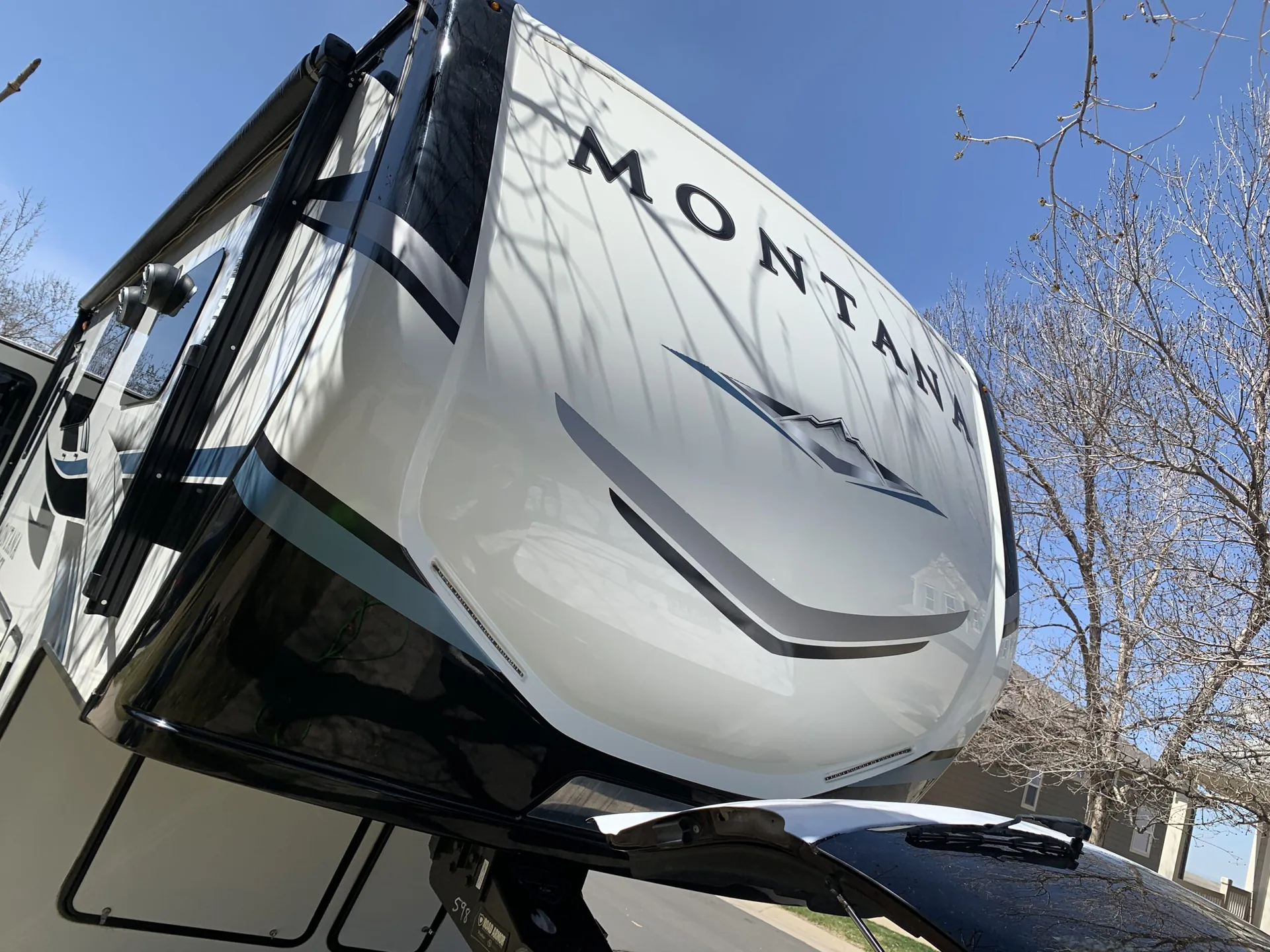 Glossy white front cap of a Montana fifth-wheel trailer from a low angle, reflecting the sky