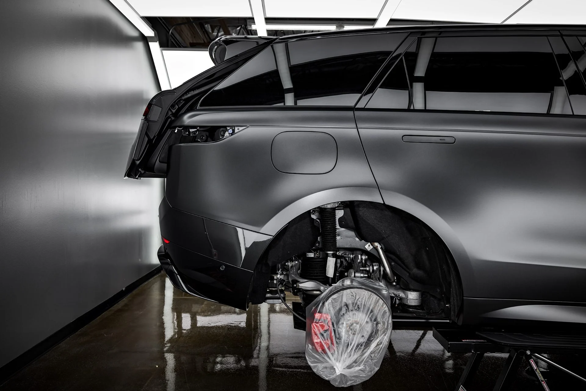 Matte black Range Rover Sport mid-wrap with a rear wheel off, vinyl being laid around the arch