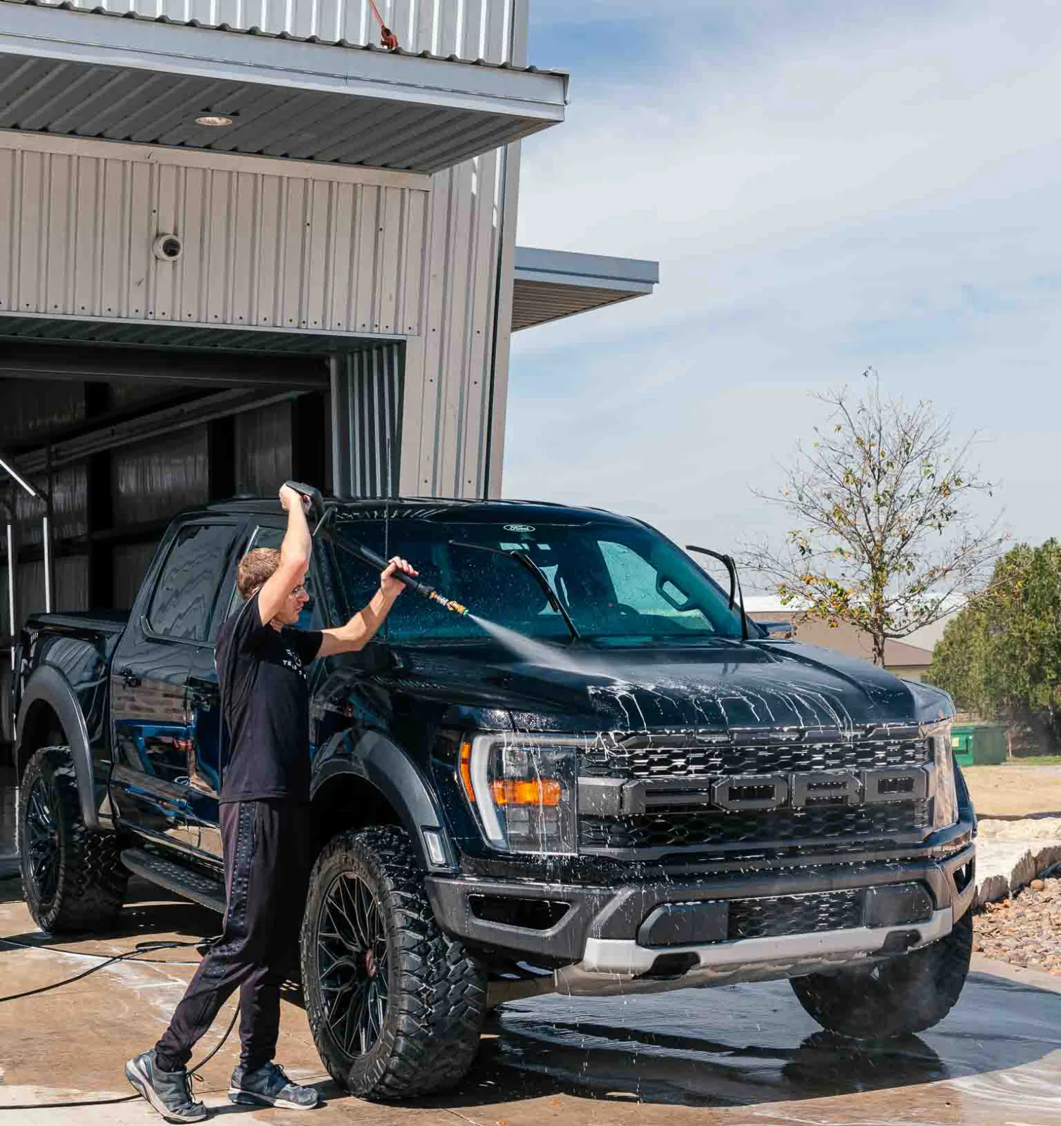 Detailer washing a black Ford F-150 Raptor outside the shop