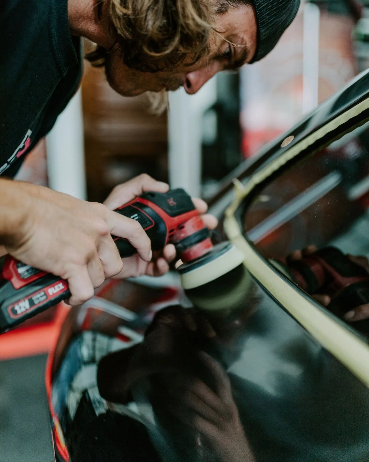 Detailer machine polishing black paint beside taped trim