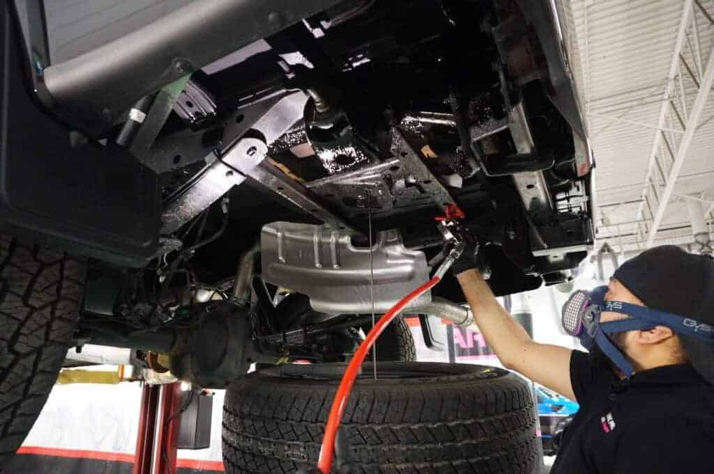 Technician spraying protective coating onto accessible vehicle underbody surfaces